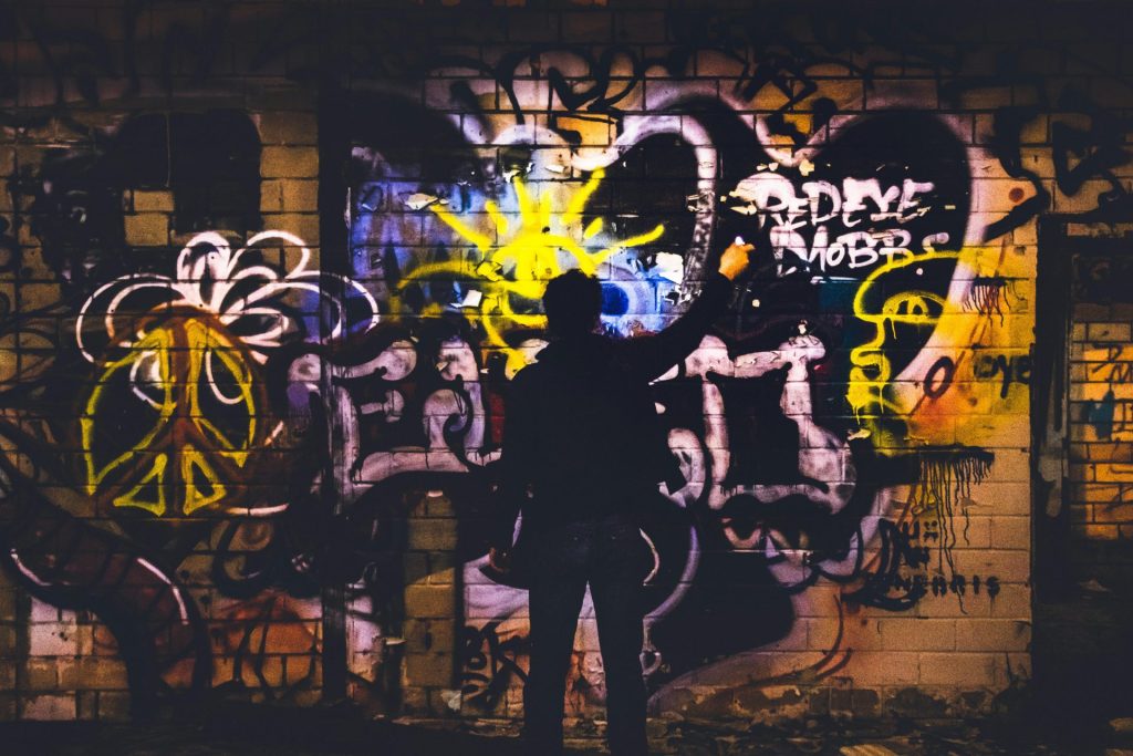 Street artist painting colorful graffiti on a brick wall at night, with vivid urban art elements.